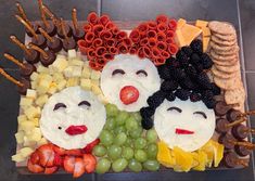 a platter with fruit, crackers and cheeses in the shape of people's faces