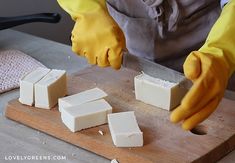 a person in yellow gloves cutting cheese on a wooden board