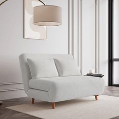 a white couch sitting on top of a wooden floor next to a wall mounted lamp