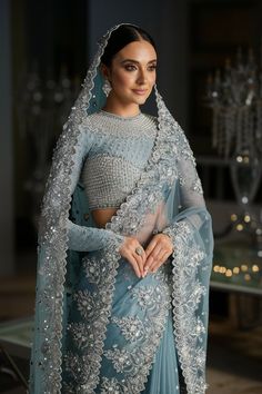 A stunning portrait of a radiant Pakistani bride wearing a pastel blue saree adorned with intricate silver threadwork and delicate floral motifs. The saree's pallu and blouse are exquisitely embellished, while the sheer detailing adds an ethereal touch. Bridal Saree With Veil, Blue And Silver Lehenga, Saree Engagement Look, Pastel Blue Saree, Reception Saree Look, Engagement Dress For Bride Indian, Engagement Dress For Bride, Reception Saree, Indian Sari Dress