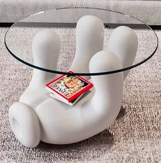 a glass coffee table with a book on it's legs and a magazine in the middle