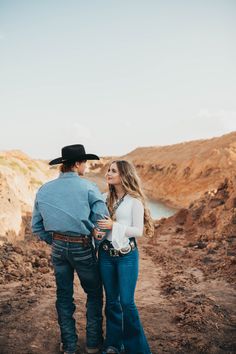 a man and woman standing next to each other on a dirt road in the desert