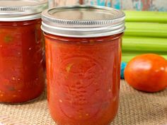 two jars filled with tomato sauce sitting on top of a table next to some vegetables