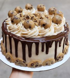 someone holding a cake with white frosting and chocolate toppings