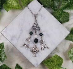 a necklace with charms on it sitting on top of a marble slab surrounded by leaves