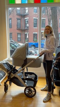 a woman standing in front of a window next to a baby carriage and stroller