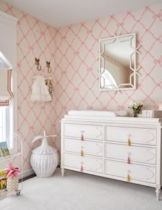 a baby's room with pink and white wallpaper, crib and dresser