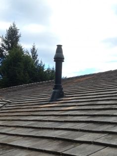 an old fashioned street light on top of a wooden shingled roof with trees in the background