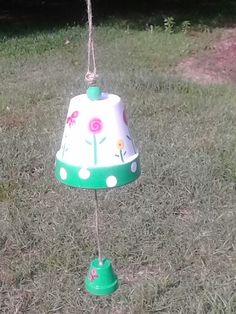 a green and white flowered lamp hanging from a rope in the grass with trees in the background