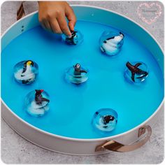 a child's hand is playing with small plastic penguins in an ice - filled tray