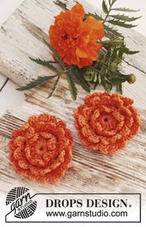 two orange crocheted flowers sitting on top of a wooden table next to an orange flower