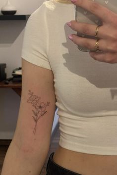 a woman with a flower tattoo on her left arm holding a cell phone in her right hand