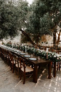 a long table set up with place settings and greenery on it for an outdoor dinner party