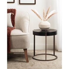 a white vase sitting on top of a black table next to a chair and framed pictures