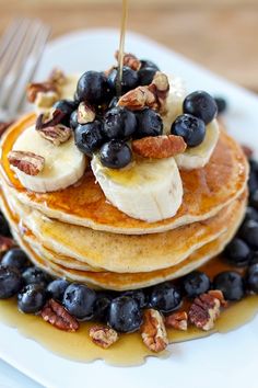 pancakes with blueberries, bananas and pecans on a plate next to a fork