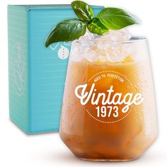 an orange drink in a glass next to a blue box with a green leaf on top