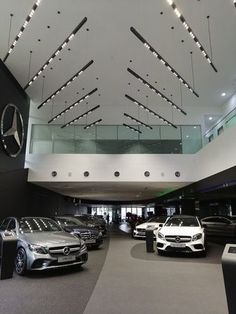 several cars are parked in a showroom with lights hanging from the ceiling above them