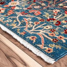 a blue area rug with red, orange and green flowers on it sitting on top of a wooden floor