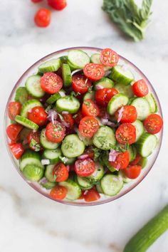 cucumber and tomato salad in a glass bowl with fresh herbs on the side