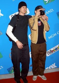 two young men standing next to each other on a red carpet holding up their cameras