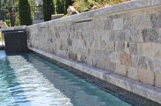 a stone wall next to a swimming pool