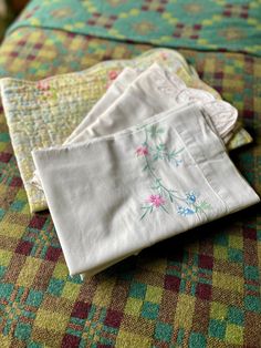 three pieces of cloth sitting on top of a bed next to each other with flowers drawn on them