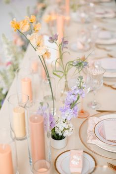 the table is set with candles, plates and vases filled with flowers on it