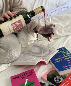 a person sitting on a bed holding a wine glass and pouring it into a book