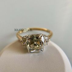 three stone ring sitting on top of a white display stand with an oval cut diamond in the center