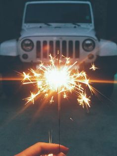 a hand holding a sparkler in front of a white jeep