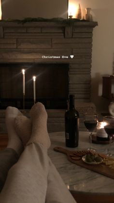 candles are lit in front of a fireplace with food and wine on the table next to it