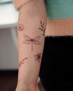 a woman's arm with dragonflys and flowers tattooed on her left arm