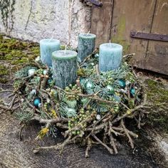 a wreath made out of branches and candles on the ground next to a building with moss growing around it