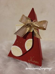 a small red christmas tree with gold bow on it's head and name written on the top