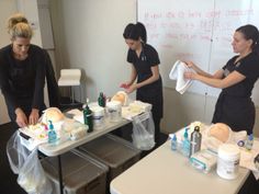 three women in black shirts and white aprons preparing food on a table with plastic bags