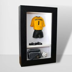 a display case with a yellow shirt and black shorts in the bottom shelf is filled with soccer memorabilia