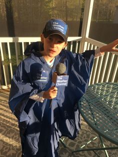 a young boy wearing a raincoat and holding a microphone in his hand while standing on a porch