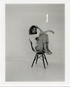 a woman sitting on top of a chair in a white shirt and shorts with her legs crossed