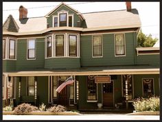 a large green house with an american flag on the front porch and two story windows