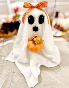 a stuffed ghost with a pumpkin in it's mouth sitting on top of a table