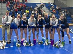 a group of young women standing next to each other on a blue wrestling court with their hands in the air