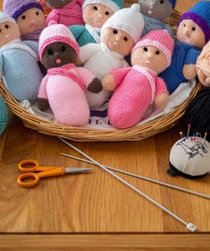 a basket filled with knitted dolls sitting on top of a wooden floor next to knitting needles