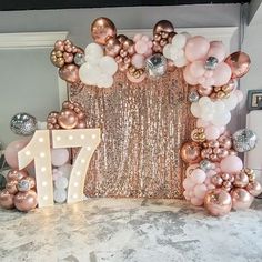 a table topped with balloons and a large number 17 balloon arch filled with pink, white and gold balloons