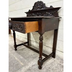 an old wooden desk with carvings on the top and bottom, sitting against a white brick wall