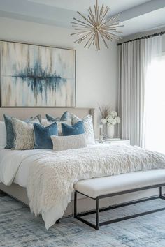 a white bed with blue and gray pillows in a bedroom next to a painting on the wall