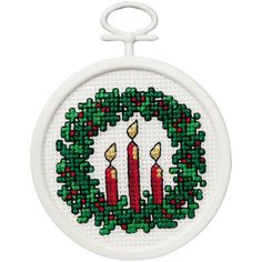 a cross stitch christmas ornament with three lit candles in a wreath on it