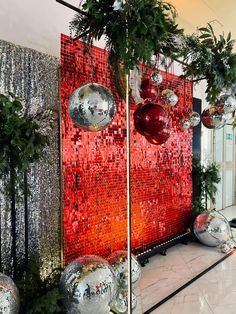 christmas decorations are displayed in front of a red and silver wall with ornaments hanging from it