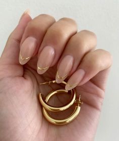 a woman's hand holding a pair of gold hoop earrings