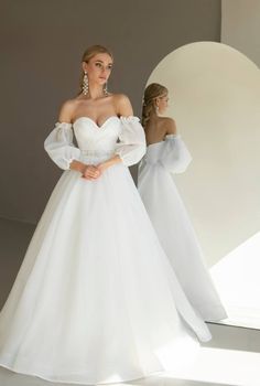 a woman in a white wedding dress standing next to another woman wearing an off the shoulder gown