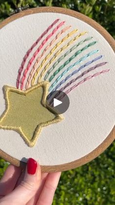 someone is holding up a hand embroidered star on a piece of wood with colored thread